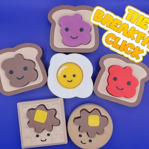 May include: Wooden breakfast-themed puzzle pieces, including toast with jam, a fried egg, and a waffle, each with a smiling face. The text "THE BREAKFAST CLICK" is in a yellow and orange banner.