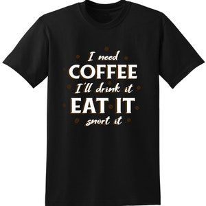 以下が含まれることがあります： 黒いTシャツに白い文字で「コーヒーが必要だ 飲む 食べる 鼻から吸い込む」と書かれている。文字の周りは小さな茶色のコーヒー豆の画像で囲まれている。