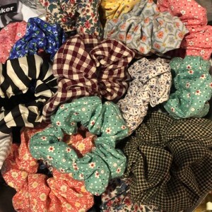 Puede incluir: Una colección de scrunchies de tela coloridos con varios patrones, incluyendo lunares, cuadros y estampados florales.