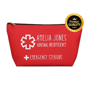 Pode incluir: Uma bolsa vermelha com zíper com texto branco e um símbolo médico. O texto diz "AMELIA JONES ADRENAL INSUFFICIENCY + EMERGENCY STEROIDS". Um selo dourado "Premium Quality" está no canto superior direito.