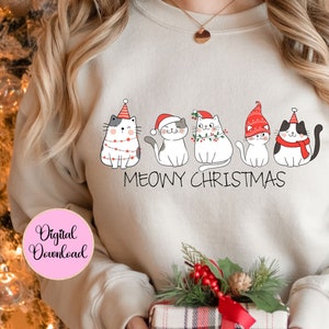 May include: Cream-coloured sweatshirt with a Christmas-themed design of five cartoon cats wearing festive hats and scarves. The words "MEOWY CHRISTMAS" are written below the cats. A pink circle with the words "Digital Download" is in the lower left corner.
