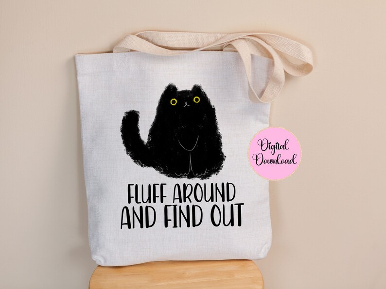 May include: White tote bag with black cat illustration and the text "Fluff around and find out".