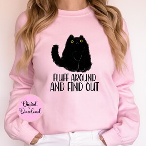May include: Pink sweatshirt with a black cat illustration and the text "Fluff around and find out".