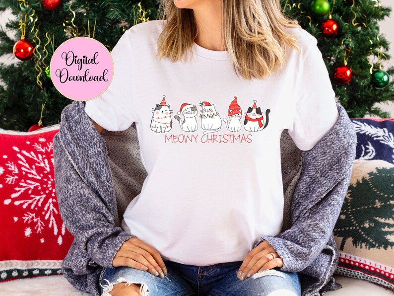 May include: White t-shirt with a "Meowy Christmas" design. The shirt features cartoon cats in Christmas hats and decorations. A pink circle with the words "Digital Download" is in the upper left corner.