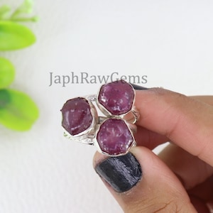 May include: A silver ring with three raw ruby gemstones. The ring is set with three faceted ruby stones, each with a unique shape and size. The ring is a statement piece that is sure to turn heads.