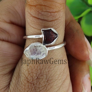 May include: A silver ring with two raw gemstones. The ring features a clear, white gemstone and a red, ruby-like gemstone.