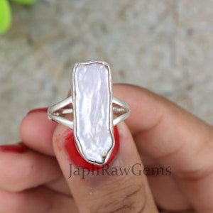 May include: A silver ring with a large, white, irregular shaped pearl. The pearl is set in a simple silver band.