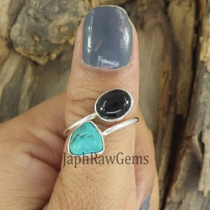 May include: A silver ring with a turquoise and black gemstone setting. The ring is worn on a person's thumb. The ring is a statement piece and would be a great addition to any jewelry collection.