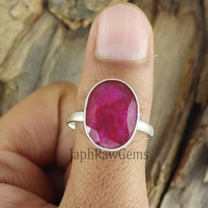 May include: A silver ring featuring a large oval ruby gemstone. The ring is worn on a finger.