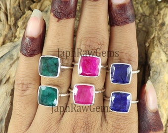 May include: Six silver rings with square-shaped gemstones. The rings feature green, pink, and blue gemstones. The rings are displayed on a hand.