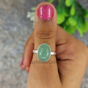 Può includere: Un anello d'argento con una pietra ovale verde chiaro. L'anello è sul pollice di una persona.