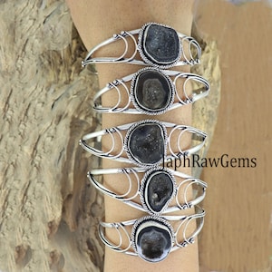 May include: Five silver bracelets with black agate stone inlays. Each bracelet features a different agate stone with a unique pattern. The bracelets are stacked on a person's wrist.