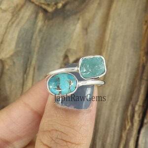 Puede incluir: Un anillo de plata con dos piedras turquesa. El anillo est&aacute; engastado con una piedra turquesa ovalada m&aacute;s grande y una piedra turquesa cuadrada m&aacute;s peque&ntilde;a. El anillo est&aacute; en un dedo.