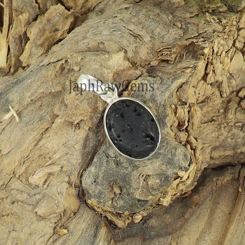 May include: A black oval lava rock pendant with a silver bail. The pendant is sitting on a piece of wood.