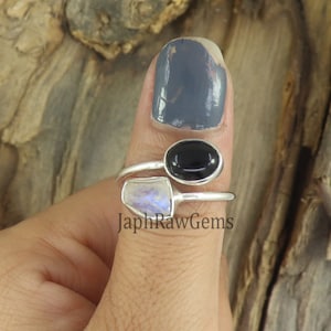 Puede incluir: Un anillo de plata con una piedra ovalada negra y una piedra blanca iridiscente. El anillo está en un dedo.