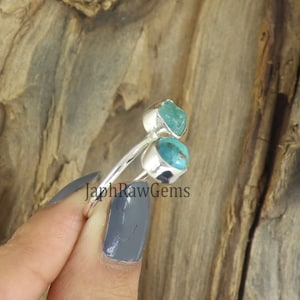 Puede incluir: Un anillo de plata con dos piedras turquesa. El anillo est&aacute; en un dedo y el fondo es de madera.