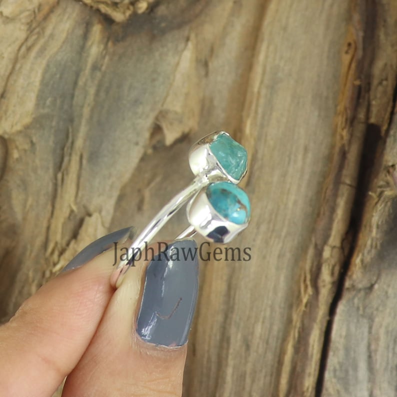 Puede incluir: Un anillo de plata con dos piedras turquesa. El anillo est&aacute; en un dedo y el fondo es de madera.