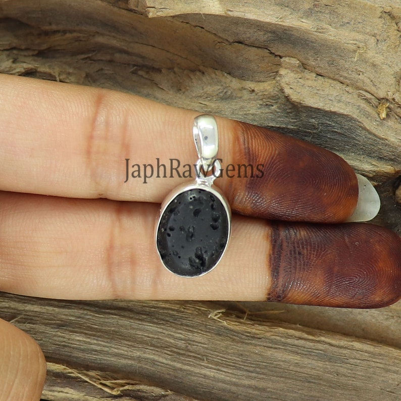 May include: A silver pendant featuring a black oval-shaped lava rock. The pendant is set in a silver bezel and has a silver bail for attaching to a chain.