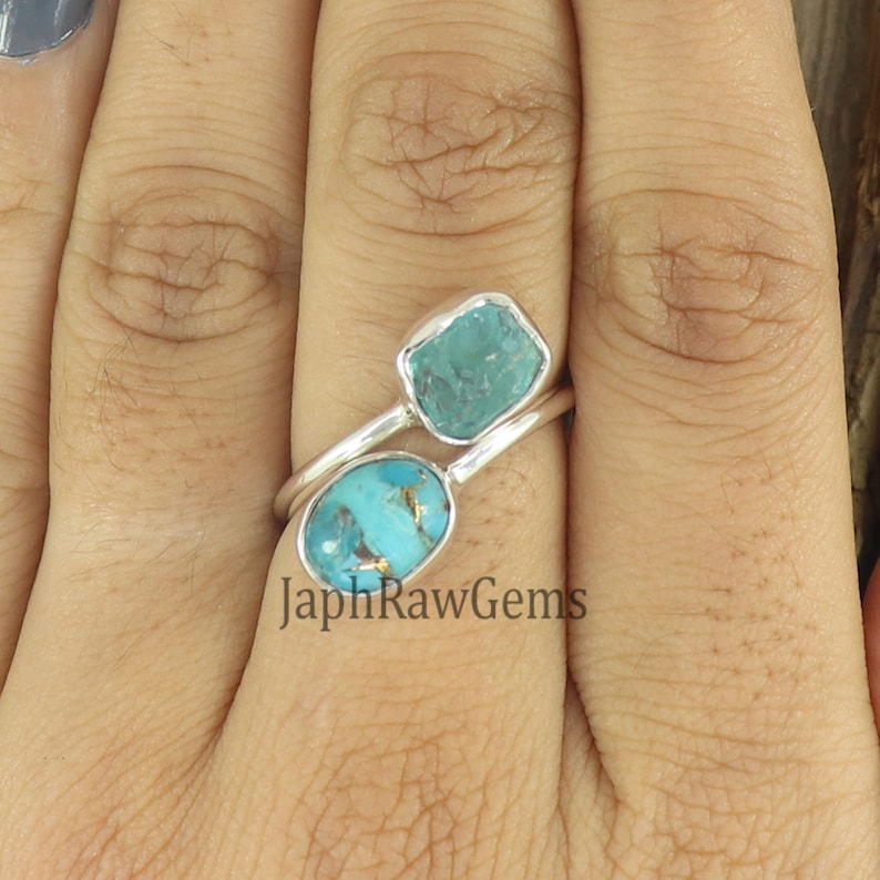 Puede incluir: Un anillo de plata con dos piedras turquesa. La piedra m&aacute;s grande es de forma ovalada y la m&aacute;s peque&ntilde;a es de forma cuadrada. El anillo est&aacute; en un dedo.