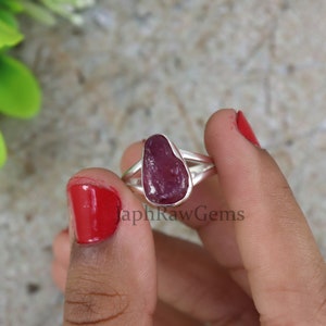 Könnte beinhalten: Ein Silberring mit einem rohen Rubin-Edelstein. Der Rubin ist tiefrot und hat eine raue, natürliche Form.