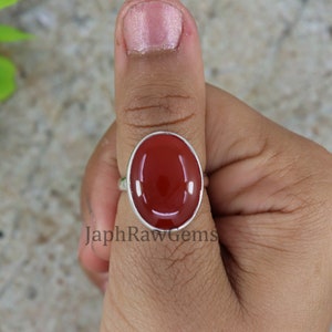 May include: A silver ring with a red oval carnelian gemstone. The ring is on a person's thumb.