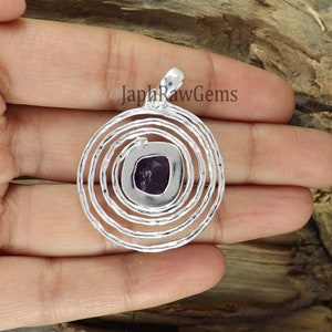 May include: A silver pendant with a purple amethyst gemstone set in a circular design with concentric circles.