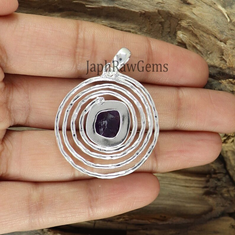 May include: A silver pendant with a purple amethyst gemstone set in a circular design with concentric circles.