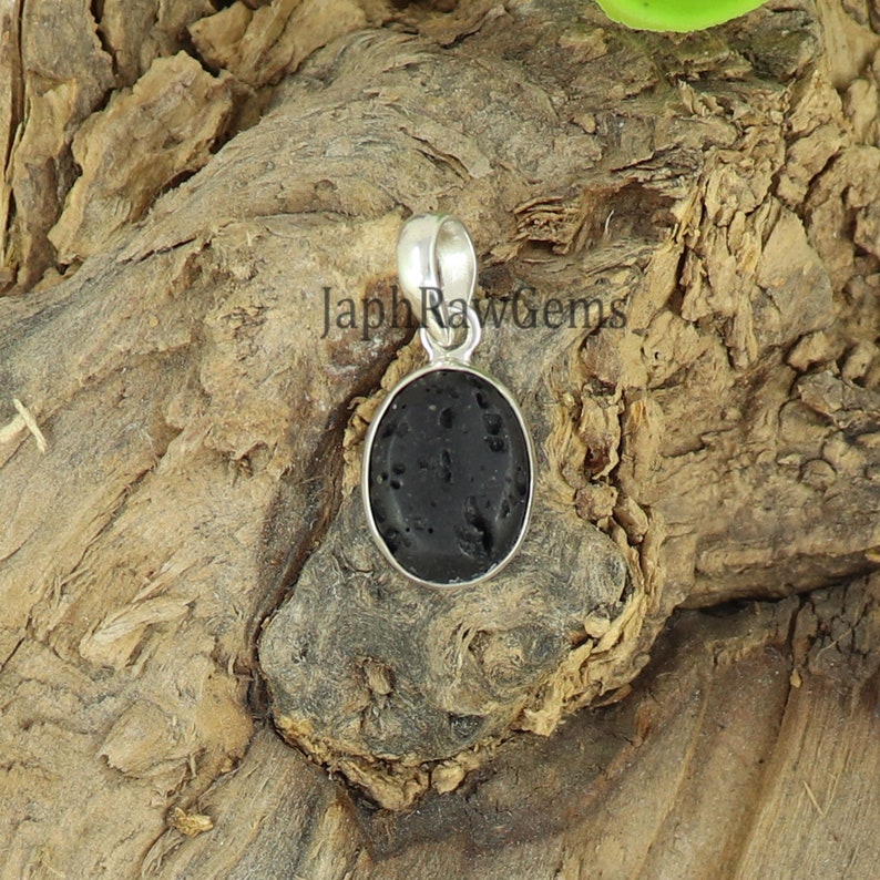 May include: A black oval lava rock pendant with a silver bail. The pendant is on a wooden surface.