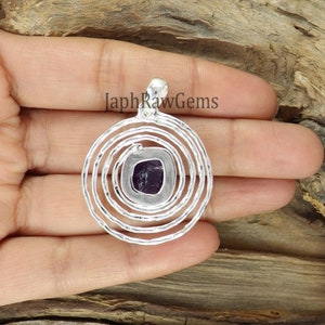 May include: A silver pendant with a purple amethyst stone set in a circular design with concentric circles.