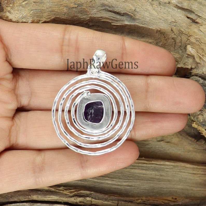 May include: A silver pendant with a purple amethyst stone set in a circular design with concentric circles.