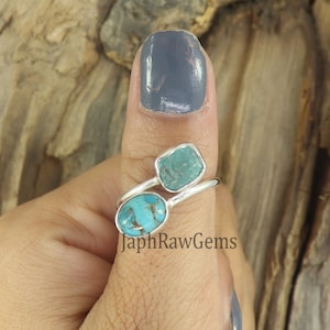 Puede incluir: Un anillo de plata con dos piedras turquesa. El anillo est&aacute; en el pulgar de una persona. Las piedras son de diferentes formas y tama&ntilde;os. El anillo es de JaphRawGems.