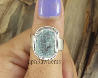 Könnte beinhalten: Ein silberner Ring mit einem großen, hellblauen Aquamarin-Edelstein, der in einer Zargenfassung gefasst ist. Der Ring wird an einem Finger getragen.