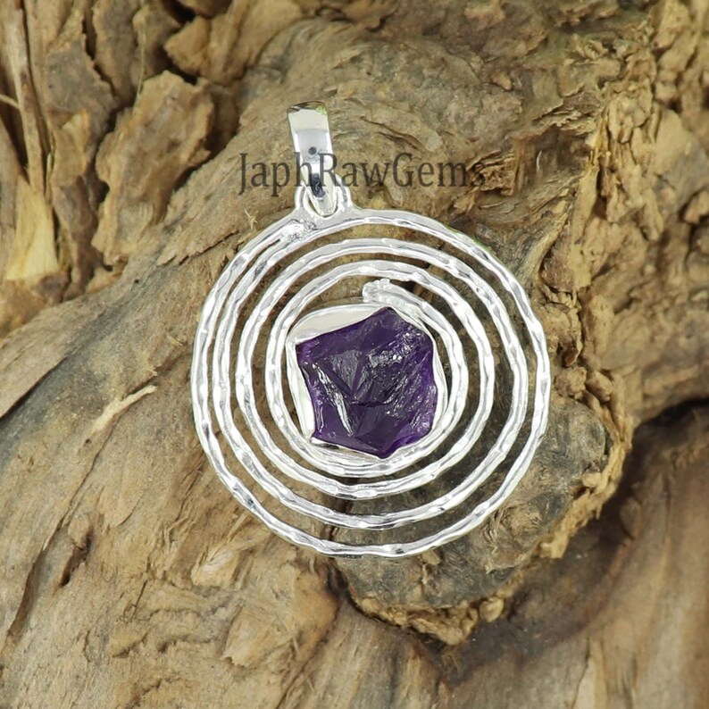 May include: A silver pendant with a spiral design and a purple amethyst gemstone in the center.  The pendant is on a wooden surface.