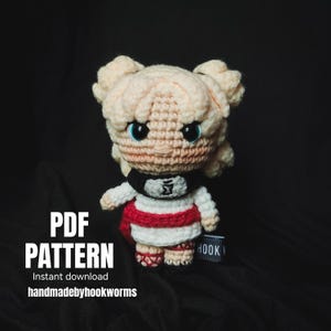 Puede incluir: Muñeca de ganchillo con cabello rubio claro, ojos azules y una diadema negra con un símbolo. La muñeca viste un atuendo blanco y rojo. La imagen incluye el texto "PDF PATTERN" y "Instant download handmadebyhookworms".