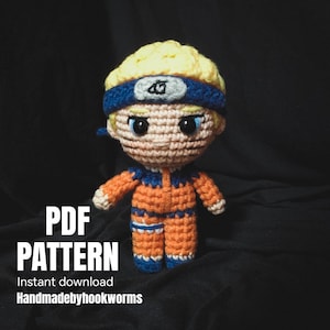 May include: A crocheted doll in an orange jumpsuit with blue accents, a blue headband, and yellow hair. The doll has black eyes and is standing against a dark background. Text on the image reads "PDF PATTERN" and "Instant download Handmadebyhookworms."