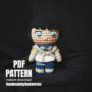 May include: A crocheted doll with black hair, blue eyes, and a white jacket with blue and yellow accents. The doll is wearing blue and white trousers. Text on the image reads "PDF PATTERN Instant download Handmadebyhookworms."