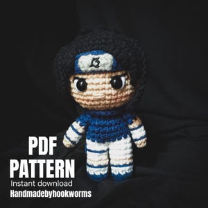 May include: A crocheted doll of a character with black hair, a blue headband, and a blue and white outfit. The doll has large black eyes and is set against a dark background. Text on the image reads "PDF PATTERN Instant download Handmadebyhookworms."