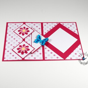 May include: A red and white card with a pop-up design featuring pink flowers and a blue butterfly. The card has a white background with a pink floral pattern.
