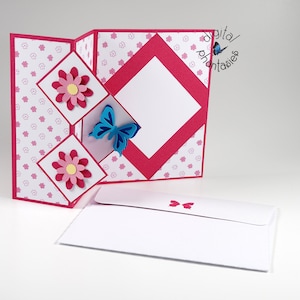 May include: A pink and white card with a pop-up design featuring a blue butterfly and pink flowers. The card is folded and has a white envelope.