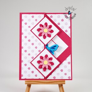 May include: A pink and white card with a butterfly and flowers. The card is folded in a unique way to create a three-dimensional effect. The card is on a small wooden easel.