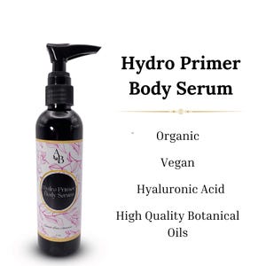 May include: A black pump bottle of Hydro Primer Body Serum with a white label and pink floral design. The label says "Hydro Primer Body Serum" and "Organic, Vegan, Hyaluronic Acid, High Quality Botanical Oils".
