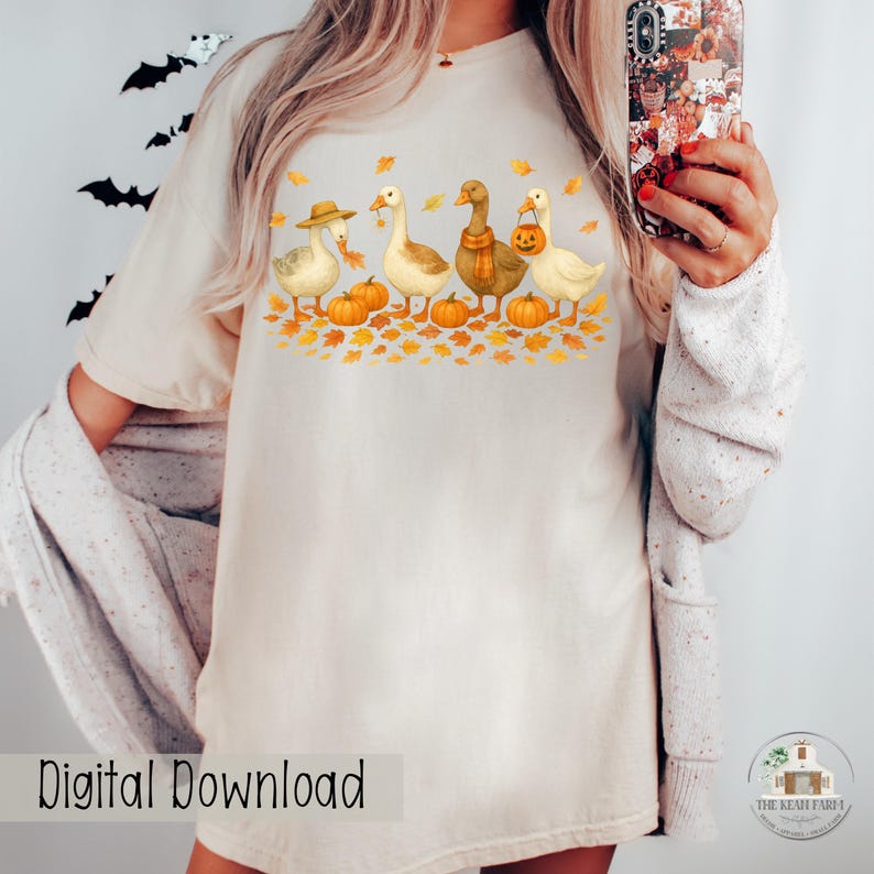 May include: Cream-colored t-shirt featuring a watercolor illustration of four geese in autumn attire. The geese are surrounded by pumpkins and fall leaves. The text "Digital Download" is at the bottom.