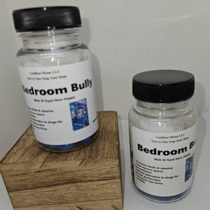 Puede incluir: Dos frascos de vidrio con tapas negras etiquetados como "Bedroom Bully". Las etiquetas incluyen texto sobre la libido y la resistencia. Un frasco est&aacute; sobre un peque&ntilde;o bloque de madera. Los frascos contienen c&aacute;psulas azules.