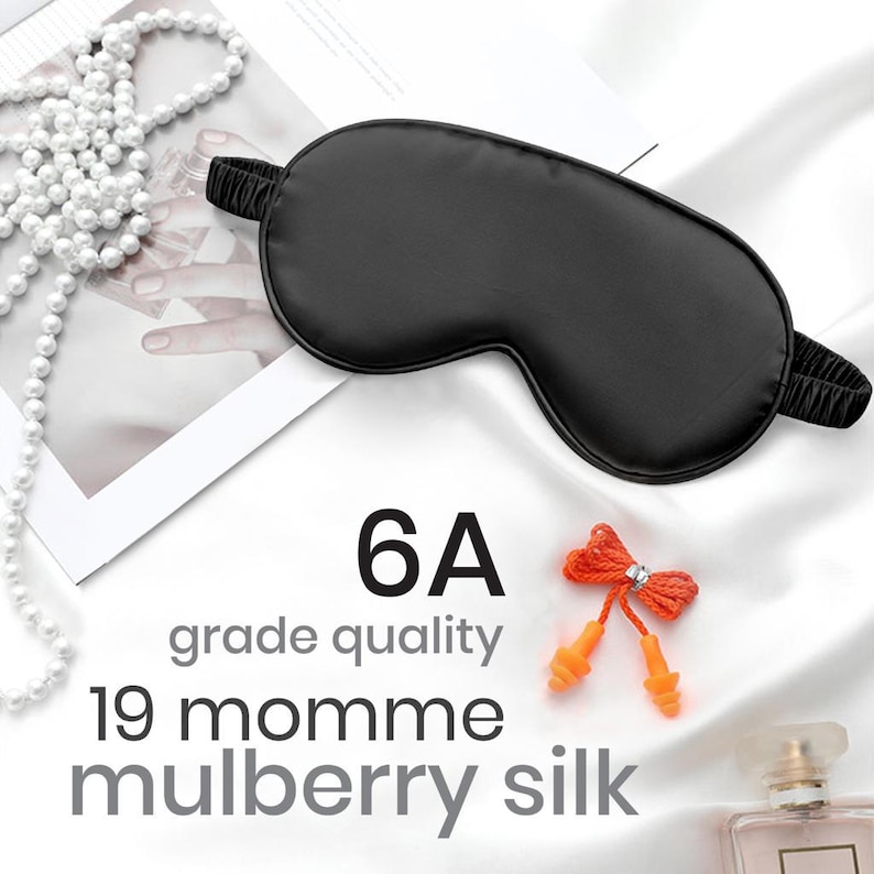May include: Black silk sleep mask with a 6A grade quality label and 19 momme mulberry silk text. The mask is on a white surface with a string of pearls and a pair of orange earplugs with a red string.