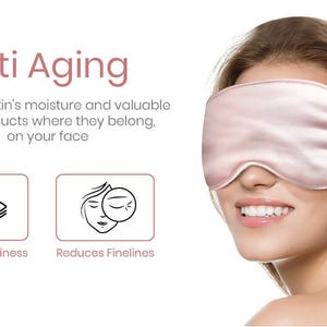 May include: A pink silk sleep mask worn by a woman with a white background. The text "Anti Aging" is above the woman's head. The text "keep your skin's moisture and valuable face products where they belong, on your face" is below the woman's head. Two icons are below the text, one showing an eye with the text "Reduces Puffiness" and the other showing a face with the text "Reduces Finelines".