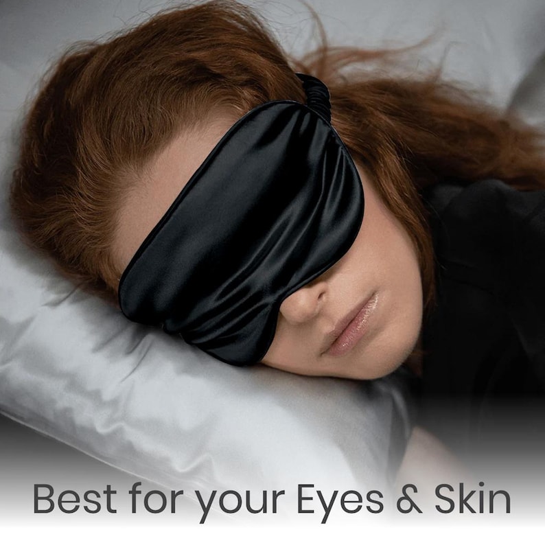 May include: A person sleeping with a black satin sleep mask over their eyes. The mask is designed to block out light and promote restful sleep.