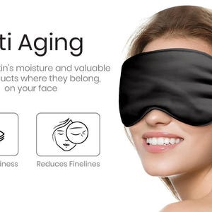 May include: A black silk sleep mask with an elastic strap. The text "Anti Aging" is above the mask. The text "Reduces Puffiness" and "Reduces Finelines" is below the mask.