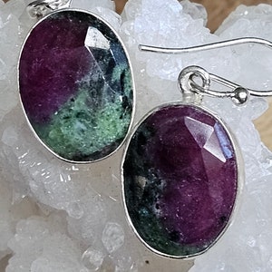 May include: A pair of silver earrings with oval-shaped green and purple gemstones. The earrings have a simple design and are perfect for everyday wear.