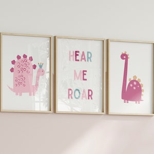 Pode incluir: Três impressões emolduradas com ilustrações de dinossauros cor-de-rosa. A impressão central mostra o texto "Hear Me Roar" em letras cor-de-rosa, azuis e verdes.