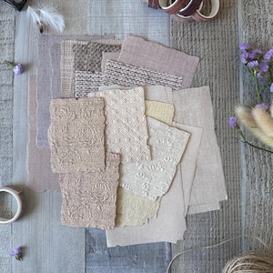 Könnte beinhalten: Eine Sammlung von Stoffmustern in neutralen Beige-, Braun- und Taupetönen mit verschiedenen Texturen und Blumenmustern. Die Stoffstücke sind in einem Stapel angeordnet und werden von mehreren Rollen Washi-Tape und getrockneten Blumen begleitet.